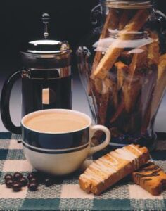large cup of cappuccino with jar of biscotti and French Press of coffee